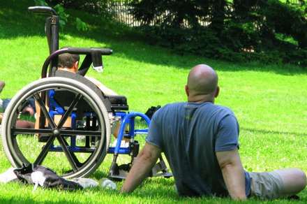 Two men on a lawn, one seated in a wheelchair
