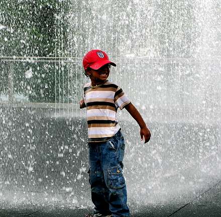 Child in a red hat running through splashing water